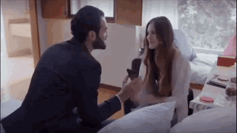 a man is kneeling down next to a woman on a bed and holding her hand .