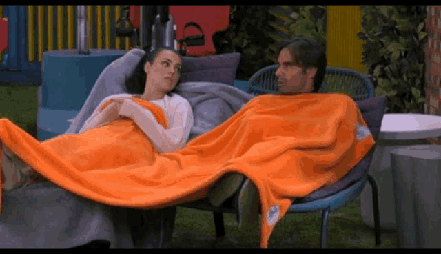 a man and a woman wrapped in orange blankets are sitting on a chair
