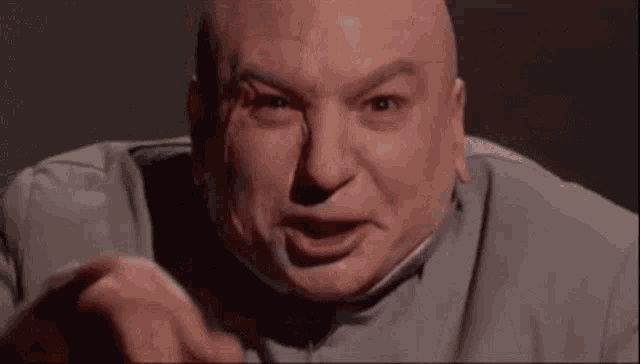 a bald man in a grey suit is making a funny face .