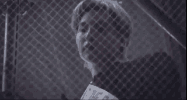 a man with blue hair is behind a chain link fence and looking at the camera .