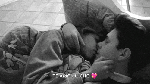 a black and white photo of a man and a woman kissing while laying on a bed .