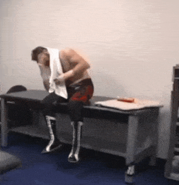 a wrestling wrestler is sitting on a bench in a locker room .