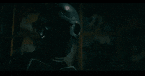 a man in a black helmet and sunglasses is standing in the dark .