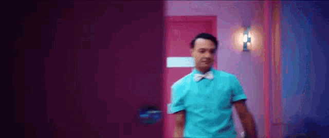 a man in a blue shirt and bow tie is walking through a pink door .