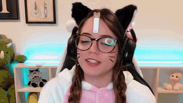 a girl wearing glasses and cat ears is sitting in a chair with her eyes closed .