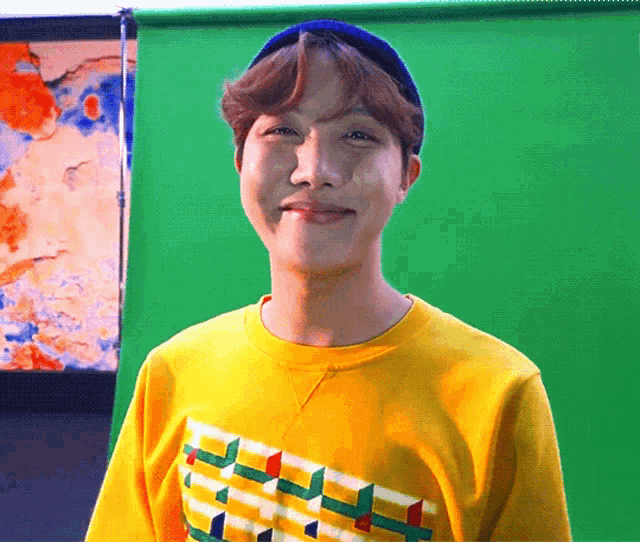 a young man wearing a yellow shirt and a blue beanie is smiling in front of a green screen .