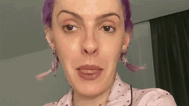 a woman with purple hair is making a funny face while wearing pajamas and earrings .