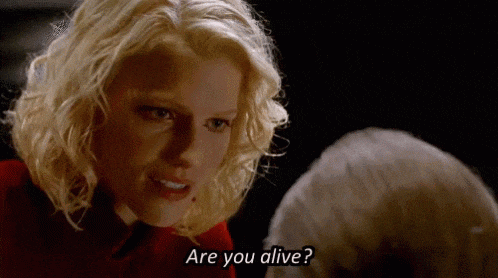 a woman is talking to a man in a dark room and asking him if he is alive .