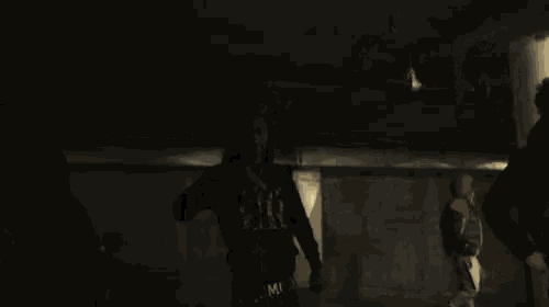two men are standing next to each other in a dark room and one has a necklace with a pendant on it