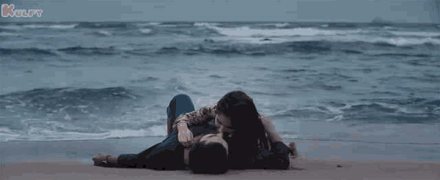 a man and a woman are laying on a beach near the ocean .
