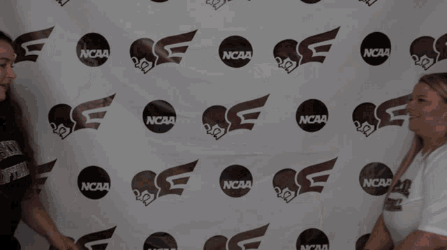 two women are standing in front of a ncaa banner