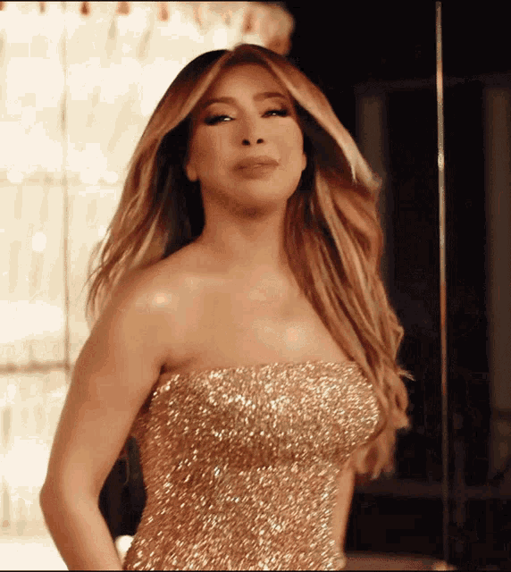 a woman in a strapless gold dress stands in front of a mirror