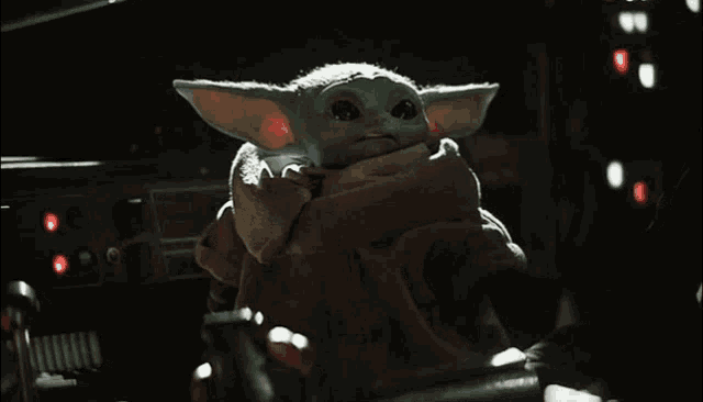 a baby yoda from star wars is sitting on a chair in the dark .