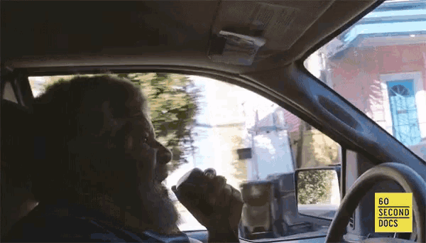 a man driving a car with a 60 second docs logo on the steering wheel
