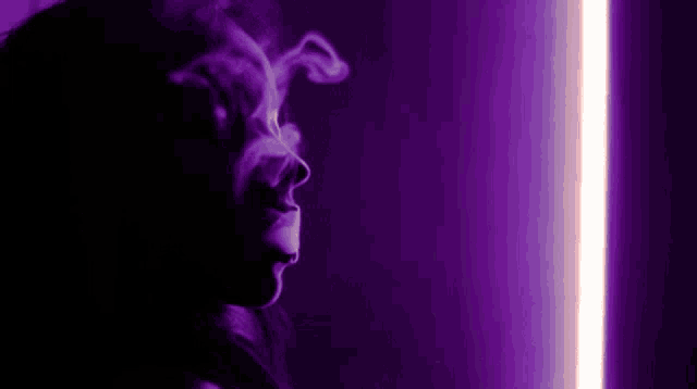a woman is smoking an electronic cigarette in a dark room with purple lights .