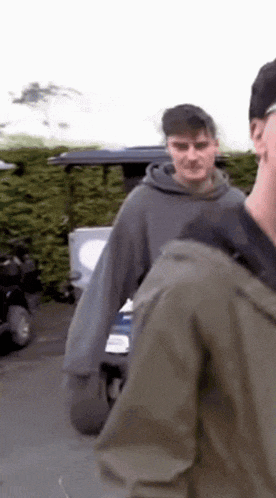 a man in a grey hoodie is standing next to another man in a green jacket .