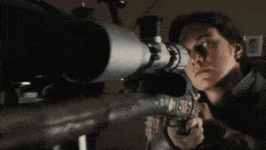 a man is looking through a telescope at something in the dark .