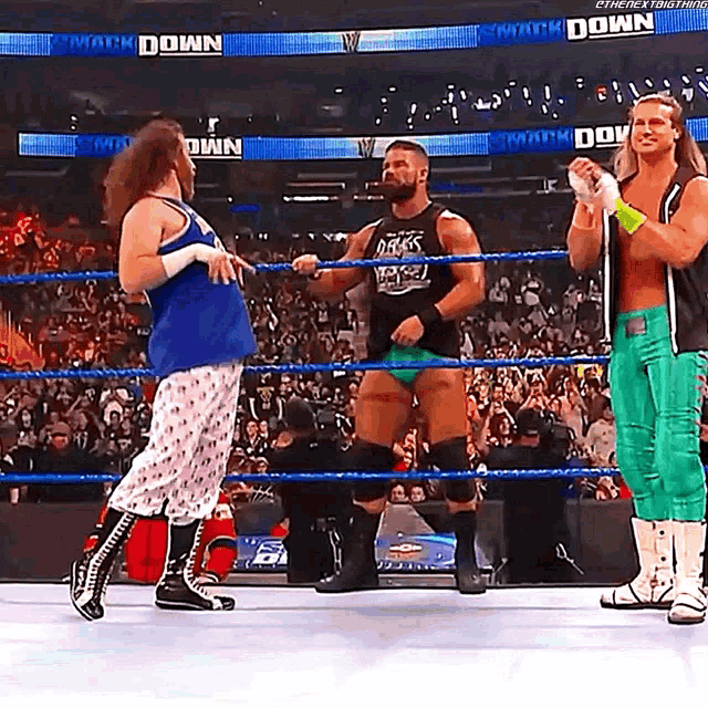three wrestlers are standing in a wrestling ring and one of them is wearing a tank top that says smack down