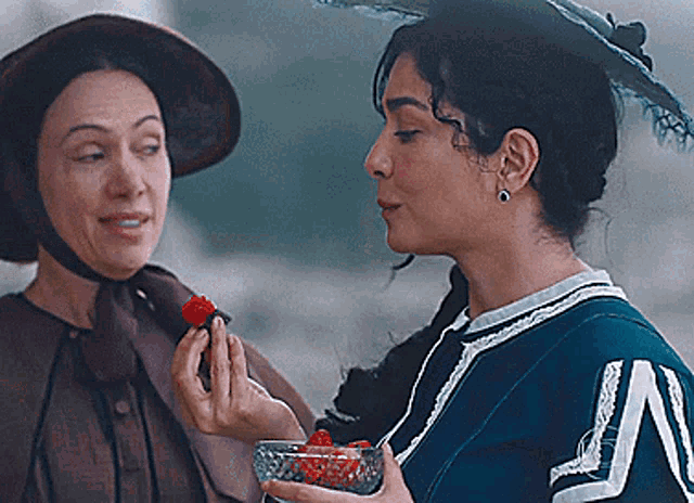 a woman is holding a bowl of strawberries and another woman is holding a flower
