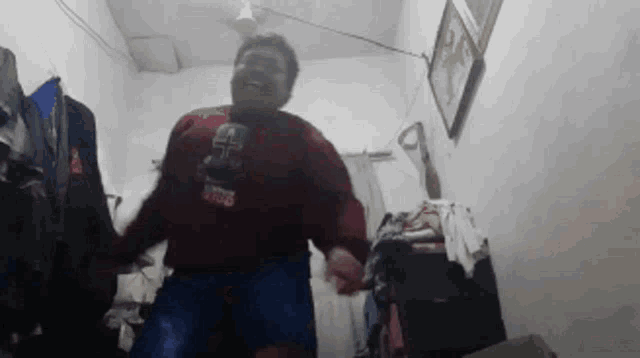 a man is dancing in a room with clothes hanging on the wall and a ceiling fan .