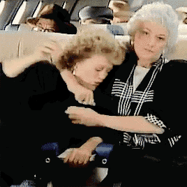 two women are sitting on a plane and one is holding the other 's neck