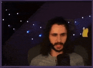 a man with long hair and a beard is sitting in front of a microphone and making a face .