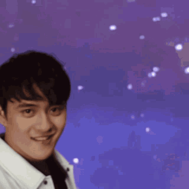 a young man in a white jacket smiles in front of a purple background