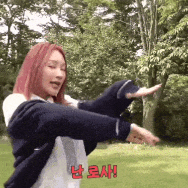 a woman with red hair is standing in a park with her arms outstretched and a foreign language behind her