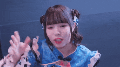 a girl in a blue dress is making a funny face with her hands