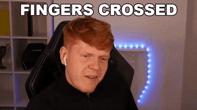 a man with red hair is sitting in a gaming chair with the words `` fingers crossed '' written on the screen .