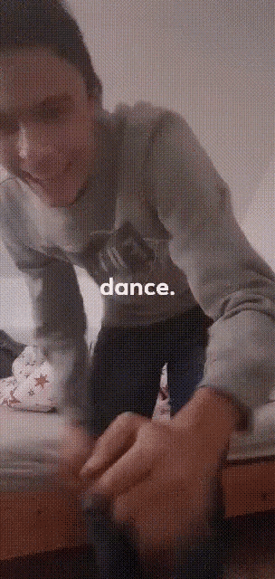a man in a grey sweatshirt is kneeling on a bed with the words dance below him