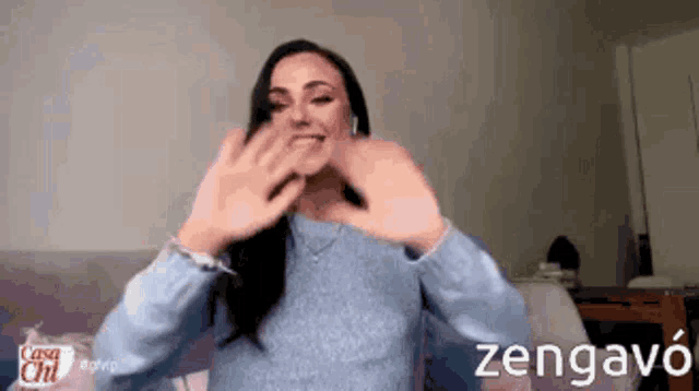 a woman wearing a blue sweater is making a heart shape with her hands