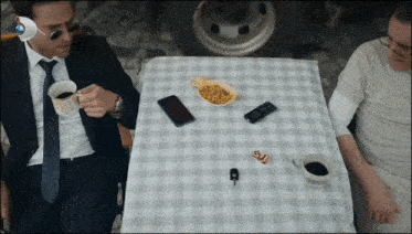 a man in a suit sits at a table with a bowl of cereal and a phone