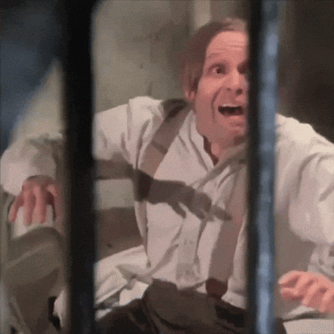 a man in a white shirt and suspenders is behind bars and making a funny face