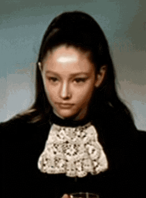 a young woman wearing a black jacket and a white lace collar is holding a glass of wine .