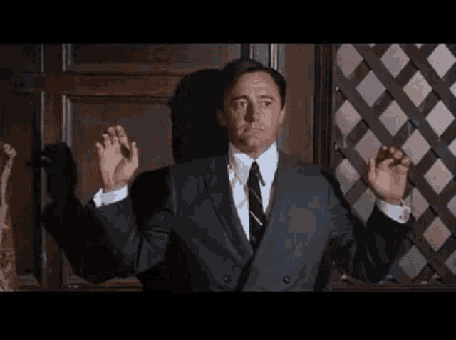 a man in a suit and tie is standing in front of a door with his hands outstretched .