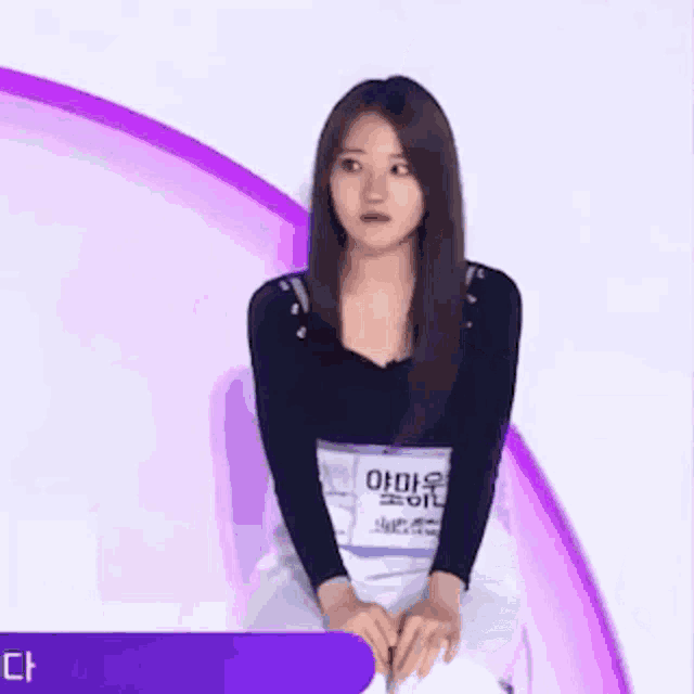 a woman is sitting on a chair in front of a purple circle with her hands on her knees .