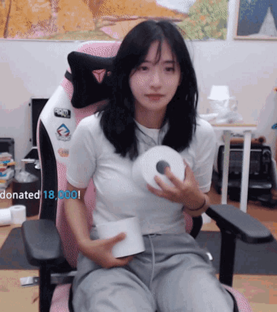 a woman is sitting in a pink chair holding a roll of toilet paper with the words donated 18,000 below her