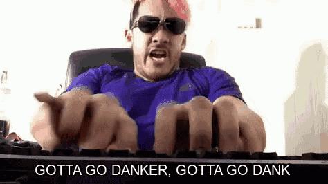 a man with pink hair and sunglasses is typing on a keyboard and making a funny face .