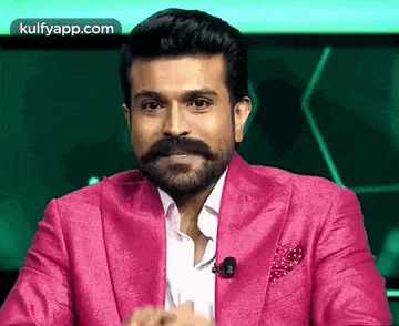 a man with a beard and mustache is wearing a pink suit and a microphone .