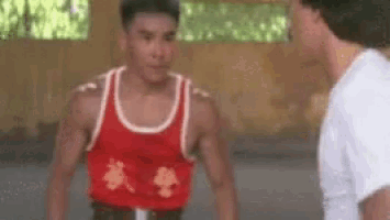 a man in a red tank top is standing next to another man in a white shirt in a room .