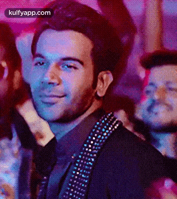 a man in a suit and tie is smiling in front of a crowd of people at a party .