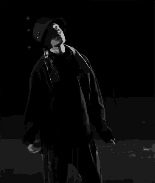 a black and white photo of a man wearing a hat and dancing in the dark .