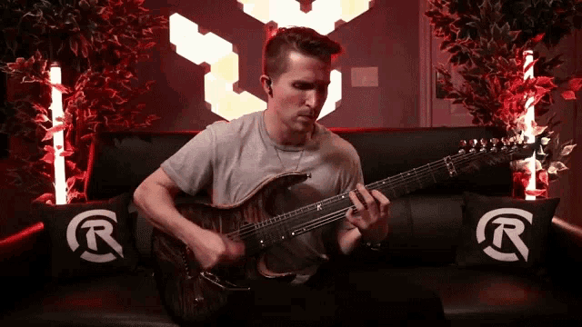 a man is playing a guitar on a couch with pillows that have r on them