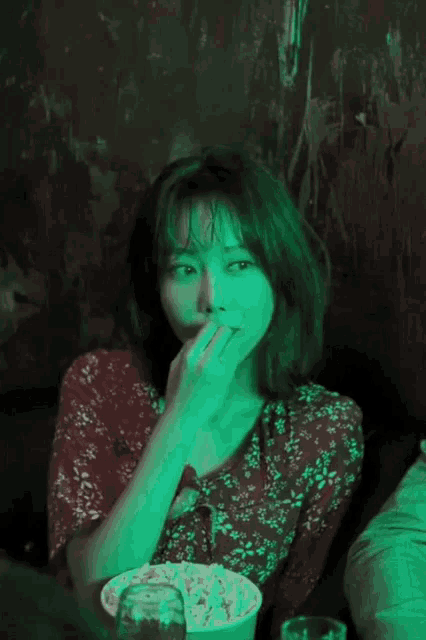 a woman in a red floral dress is eating popcorn in a dark room