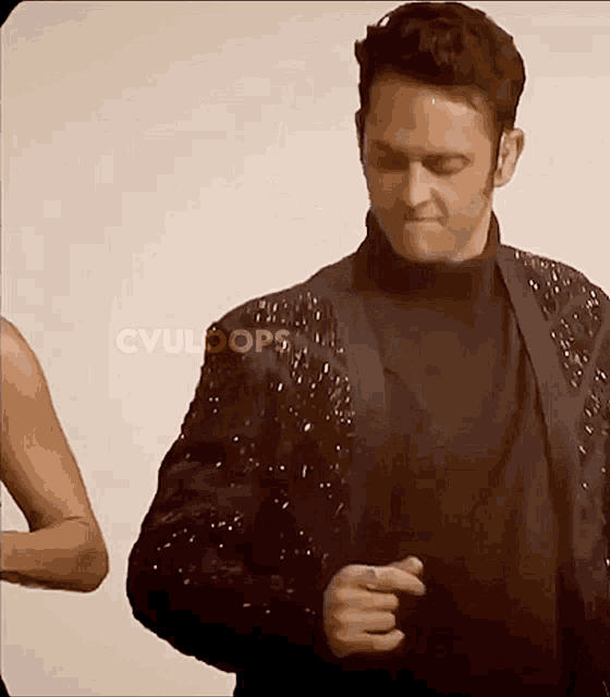 a man wearing a black jacket with sequins on the sleeves is standing in front of a cvuloops logo