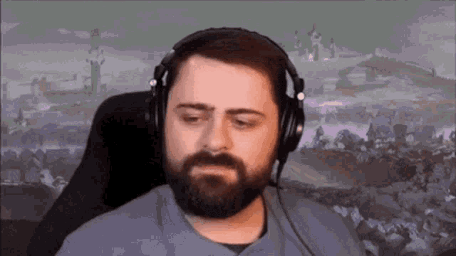 a man with a beard is wearing headphones while sitting in front of a screen .