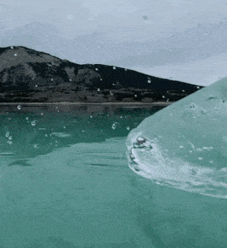 a wave is breaking in the ocean with mountains in the background