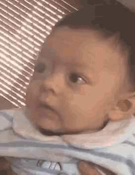 a baby in a striped shirt is being held by a person and looking at the camera .