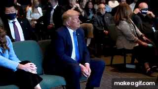 a man in a suit and tie is sitting in a chair in front of a crowd of people .